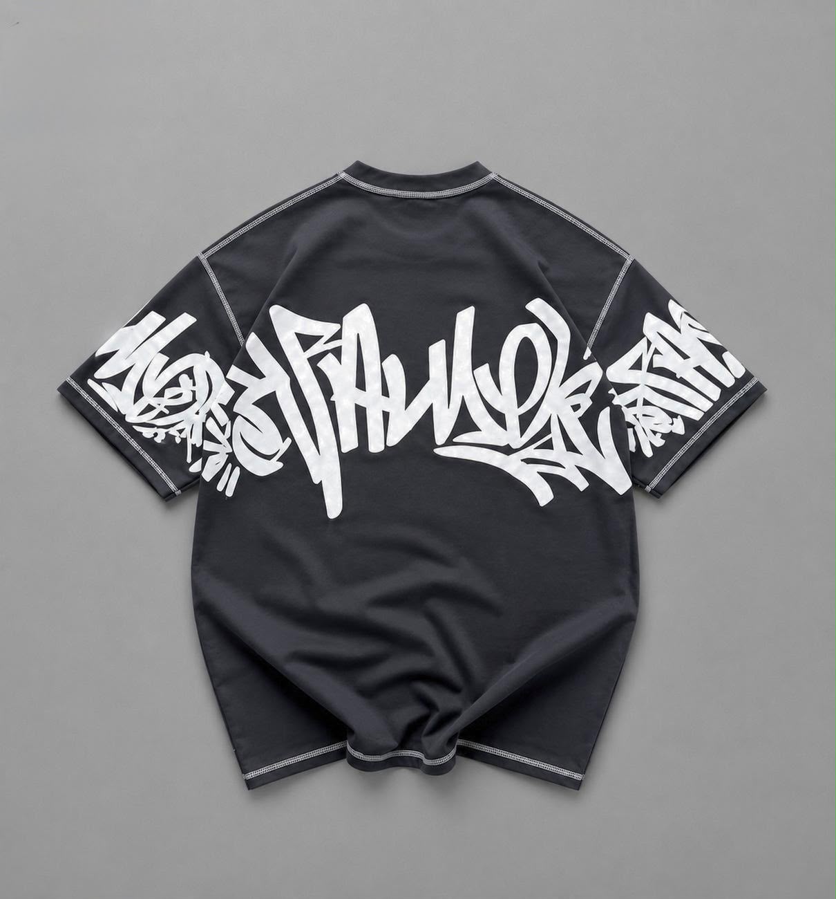A black short-sleeve t-shirt with a large white graffiti-style graphic across the back and white piping details, laid flat on a gray background.