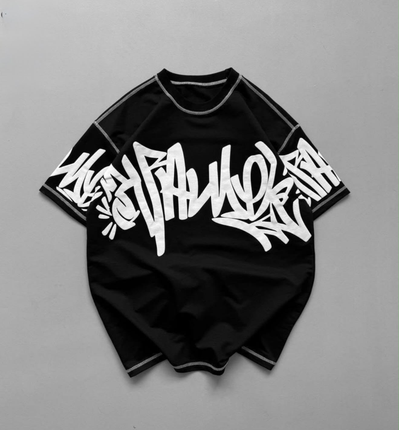 A black short-sleeve t-shirt with a large white graffiti-style graphic across the chest, laid flat on a neutral gray background.