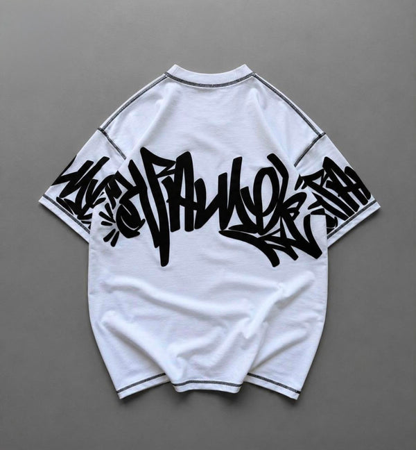 A white short-sleeve t-shirt with black graffiti-style lettering across the back and black piping on the shoulders and hem, laid flat on a gray background.