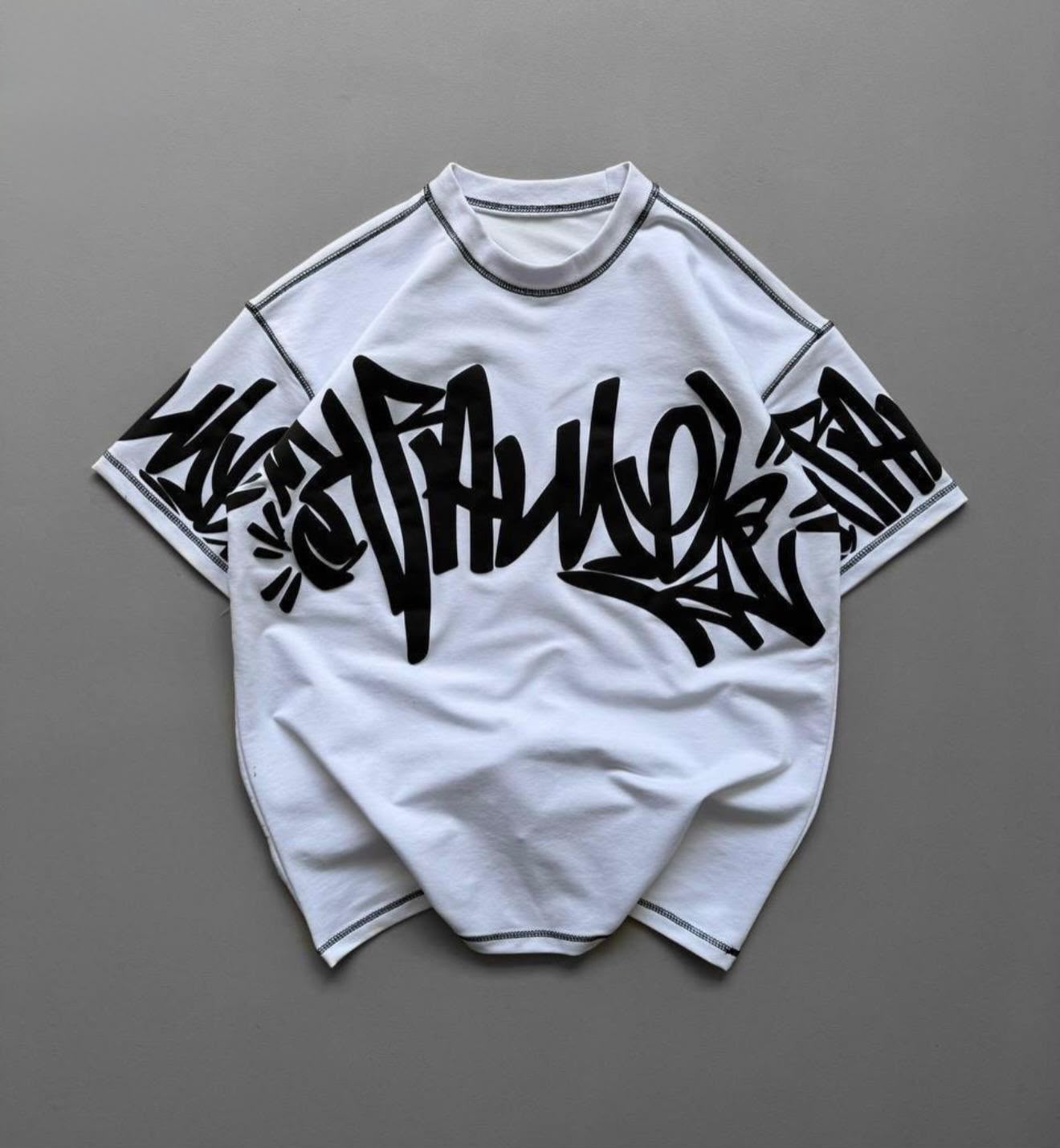 A white short-sleeve t-shirt with a large black graffiti-style graphic across the chest and sleeves, laid flat on a neutral gray background.